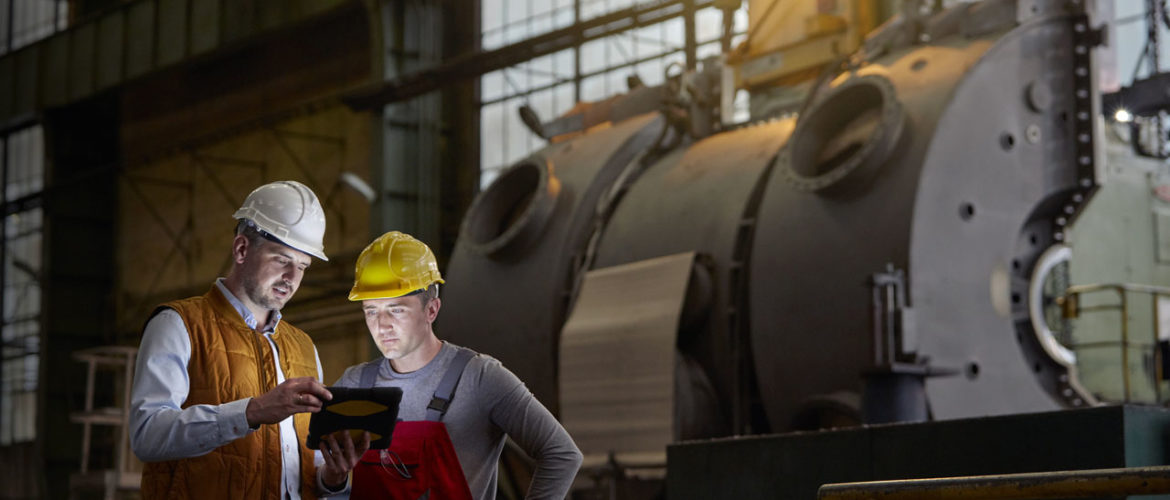 Male engineer and worker using digital tablet in dark factory